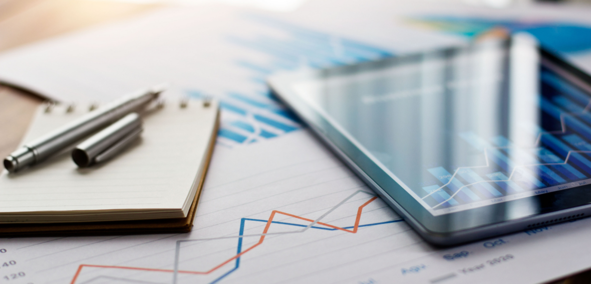 A computer tablet, notepad and pen on a desk, on top of a line graph