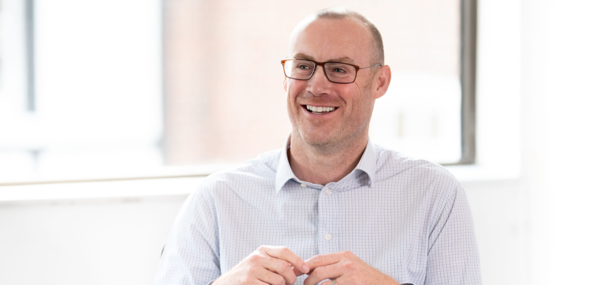 A person smiling, wearing glasses and a light-coloured professional shirt